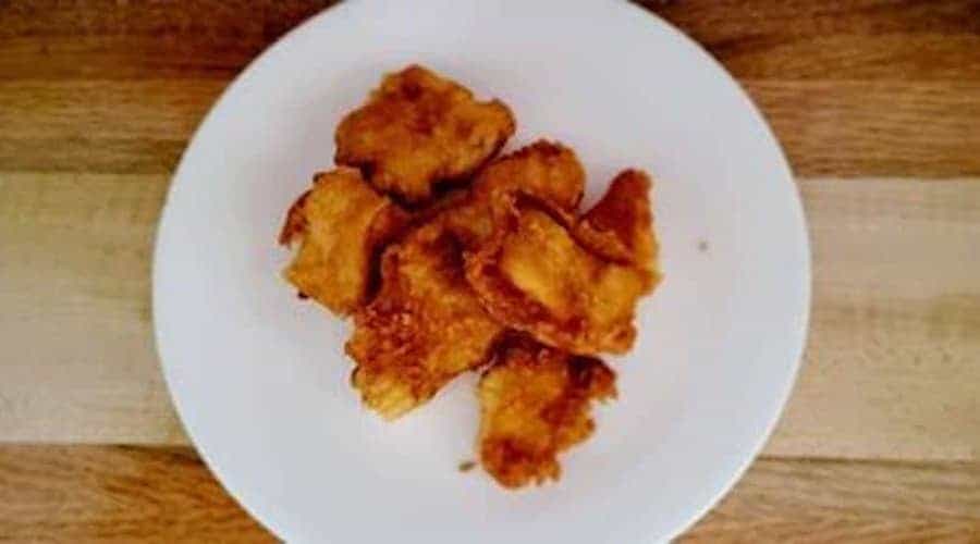 Air fried catfish nuggets on a white plate against a wooden background.