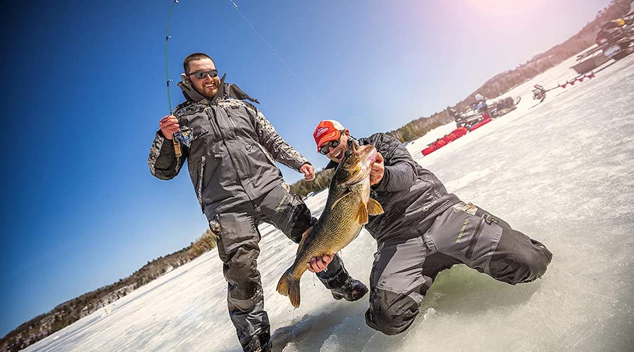 Two people ice fishing with one person holding up a fish over the ice.