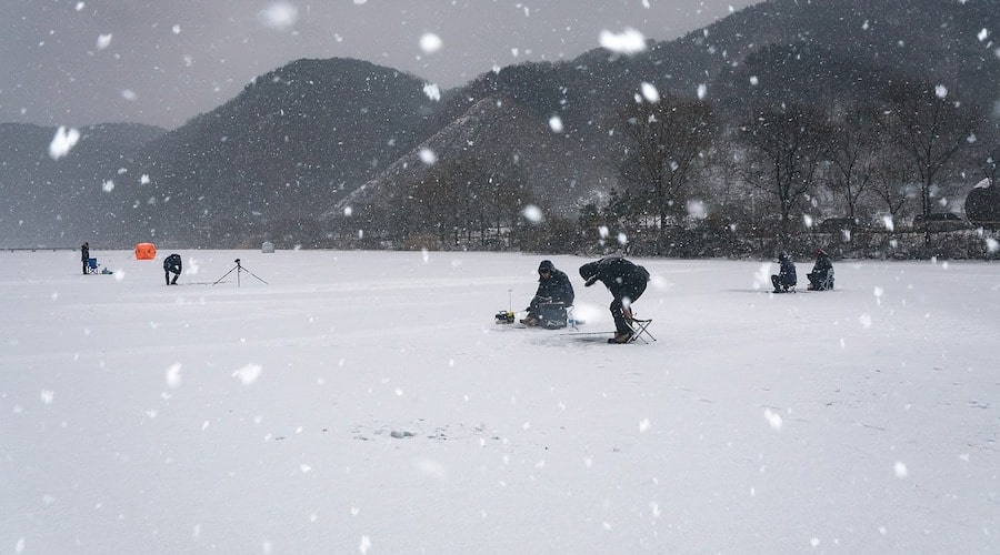 a group of people ice fishing with snow falling from the sky. 