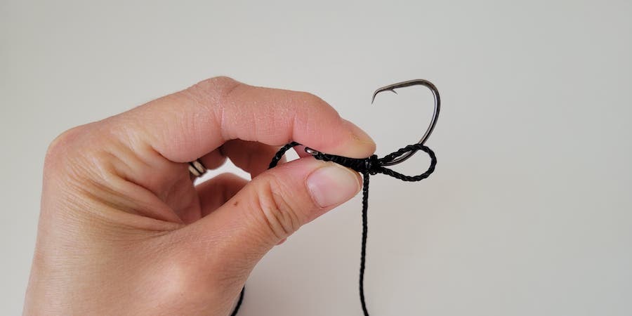 A hand holding a hook with fishing line wrapped around the shaft against a white background.