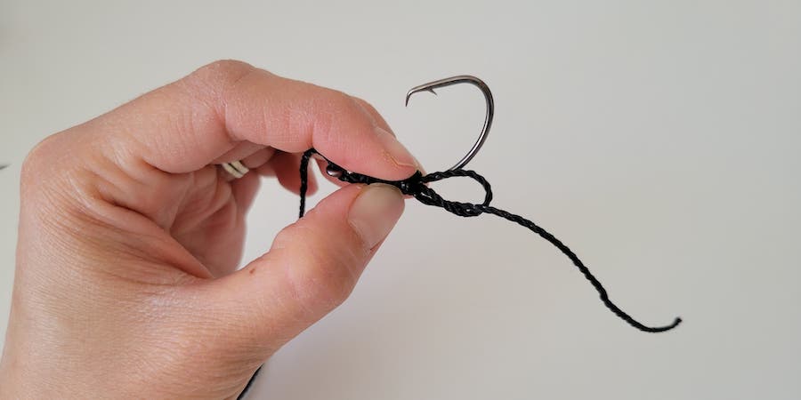 A hand holding a hook with fishing line tied around it against a white background.