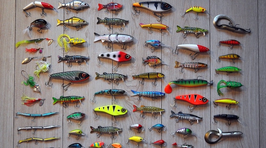 A large quantity of fishing lures laying on a wooden floor.